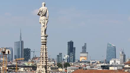 Milan skyline with skyscrapers in the distance and a Duomo tower featuring a stone archer in the foreground.